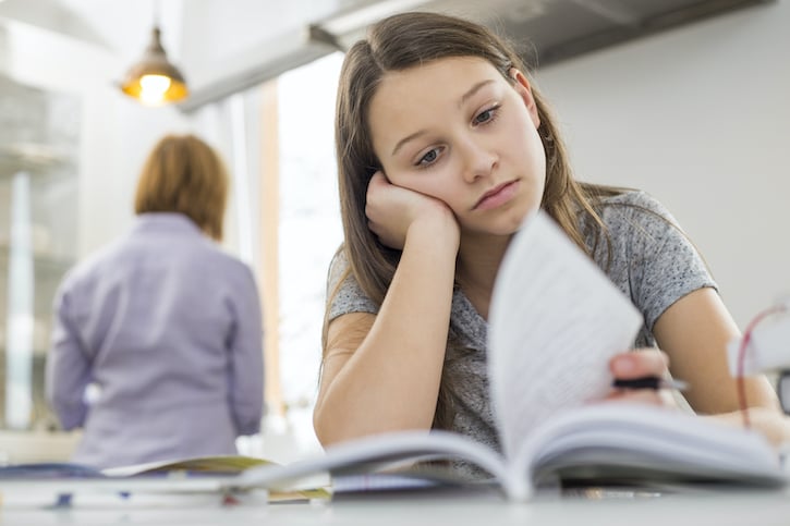 Girl studying at table with mother standing in background