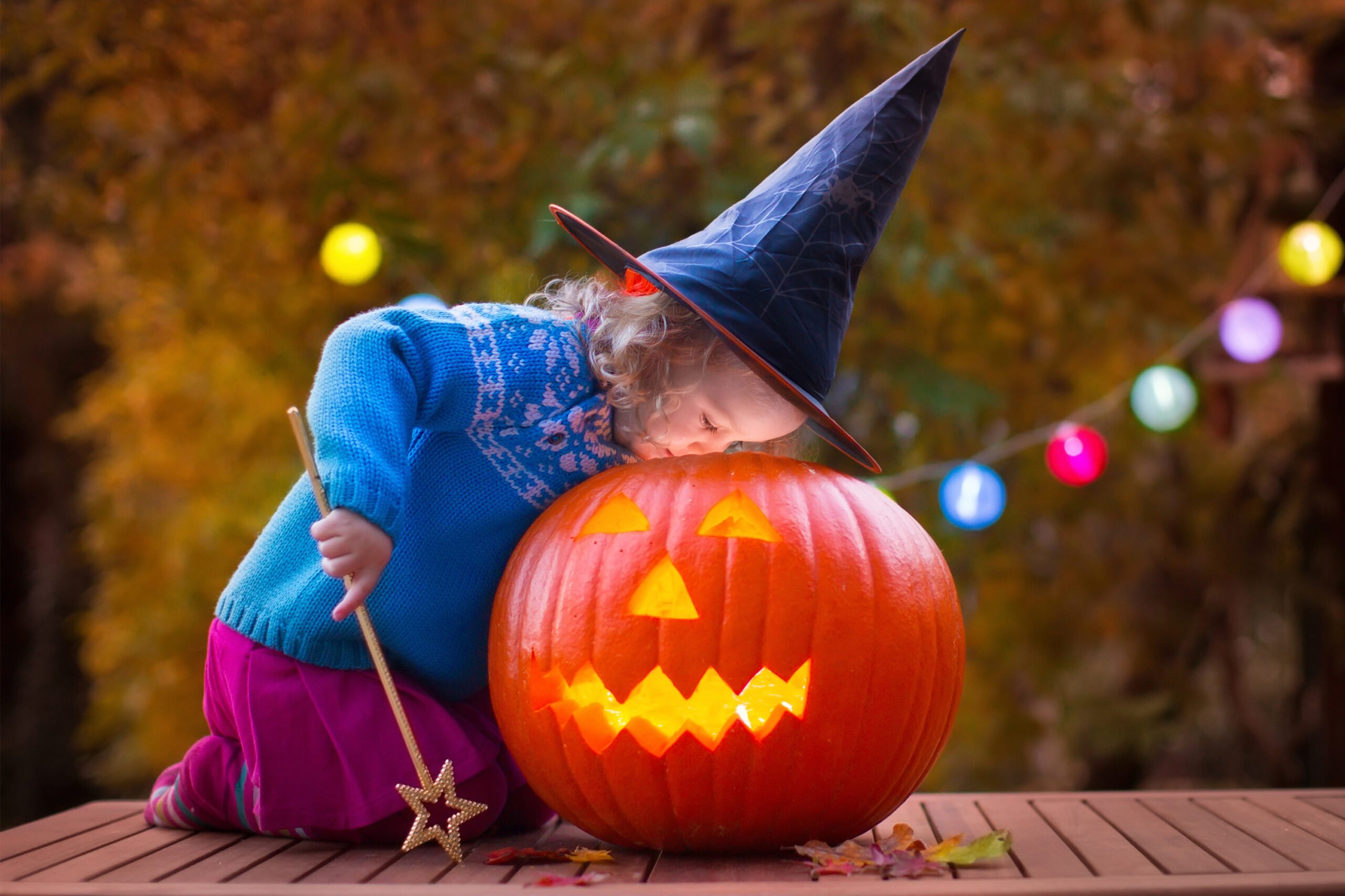 girl with witch hat and wand looking into jack o lantern pumpkin