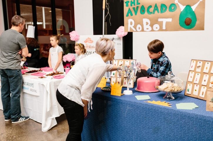 Woman looking at items for sale by boy at Acton Children's Business Fair