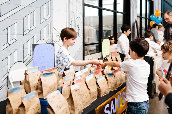 Boy behind table at Acton Children's Business Fair making sale in a brown paper bag to another boy