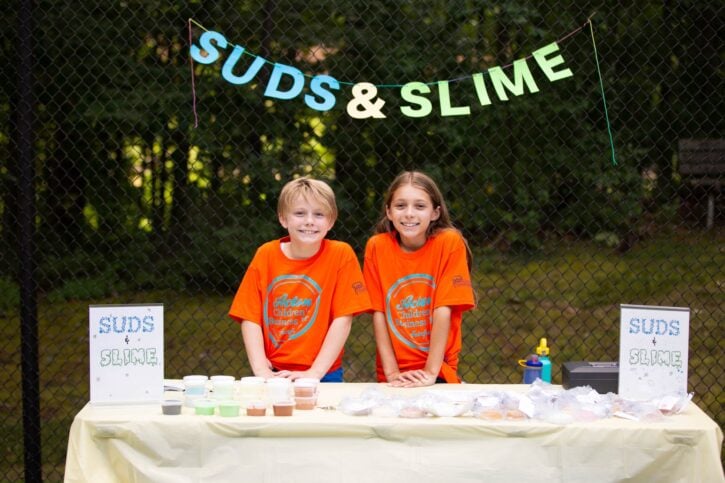 Boy and girl in orange shirts selling suds and slime at Acton Children's Business Fair