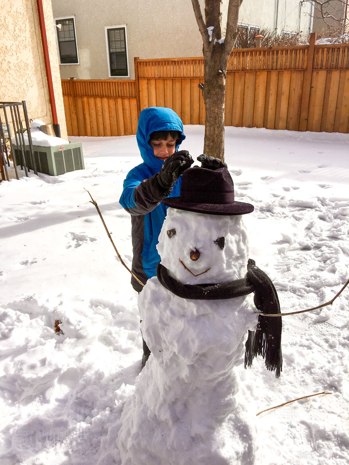 Boy in winter gear building a snowman with hat and scarf.